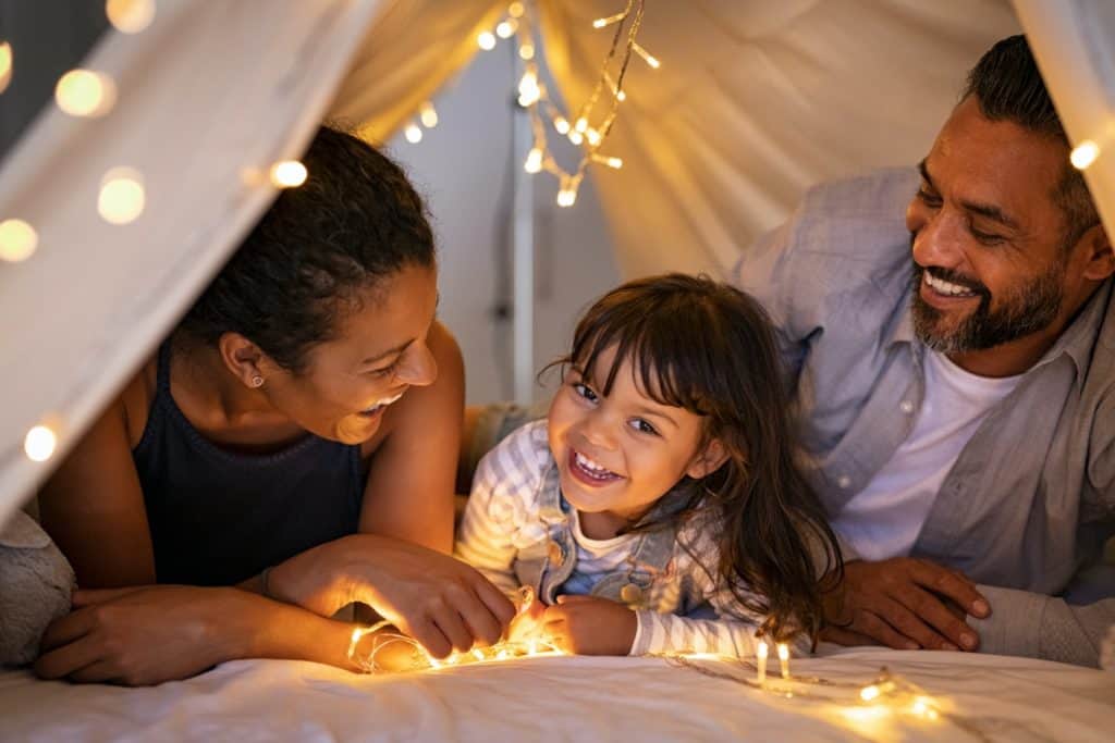 Family in home made indoor fort with Christmas lights laughing