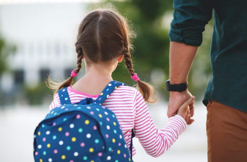 Father and daughter holding hands while walking to school